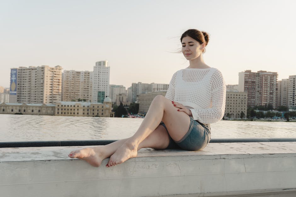 Woman enjoying peaceful moment on rooftop with city skyline in the background at sunset.