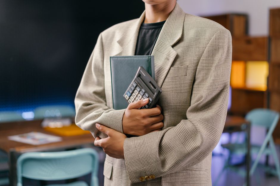 A young professional holds a calculator and notebook in an office setting.