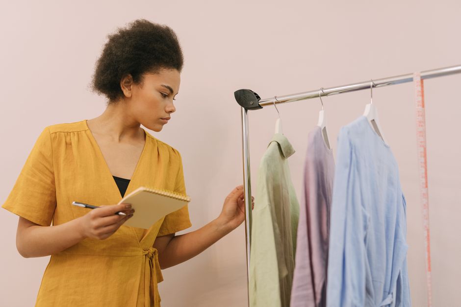 Focused young woman takes notes while examining clothes on a rack in a fashion studio.