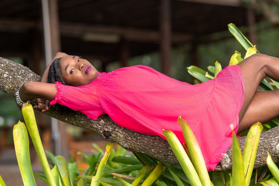A woman in a bright pink dress lounging on a tree branch in a garden setting.