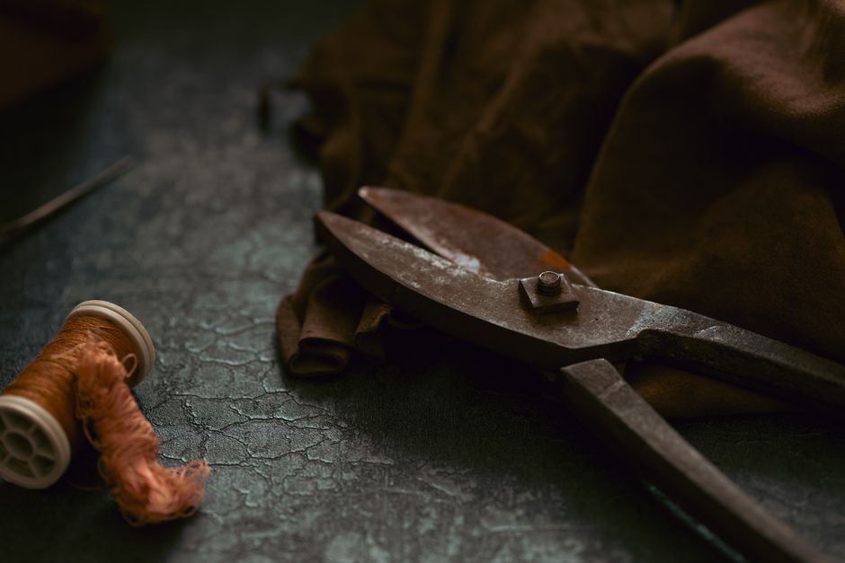 A close-up of vintage scissors, thread, and brown fabric in a moody, artistic composition.