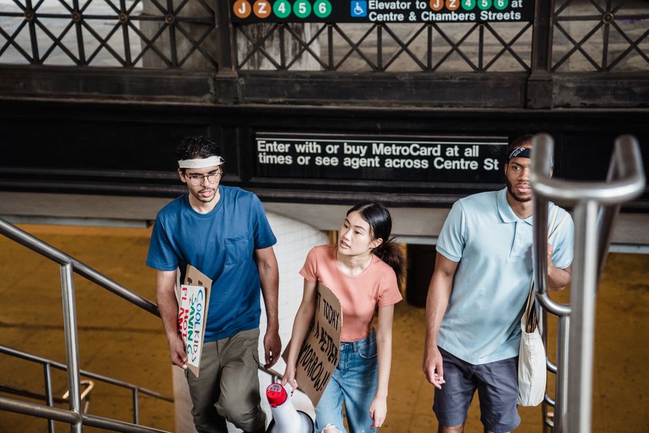 A diverse group of young adults walking in a subway station holding protest signs.