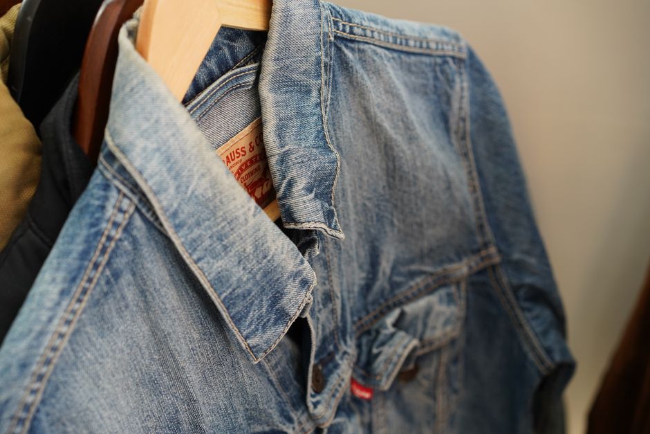 Close-up of a blue denim jacket hanging on a wooden hanger indoors.