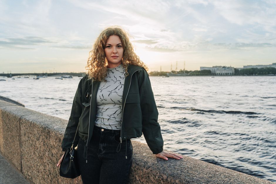 A woman stands by a river, enjoying a serene sunset on a breezy day.