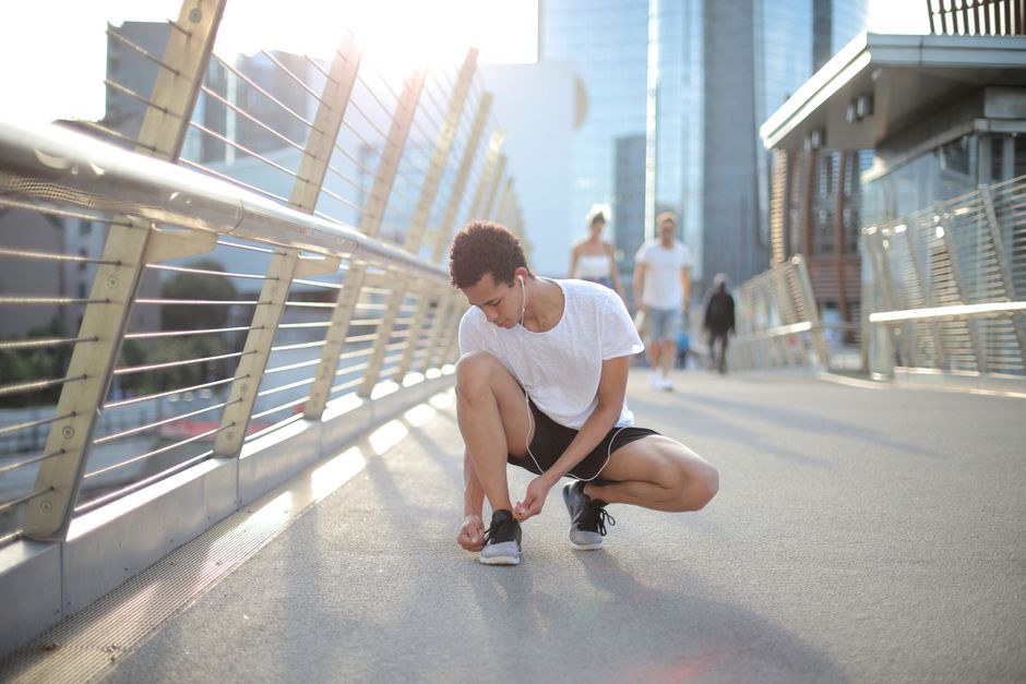 Calm crouched African American man in white shirt and black shorts lacing sneakers while preparing to run on street in downtown