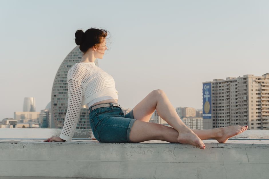 A woman in summer attire enjoying a cityscape view from a rooftop at sunset.