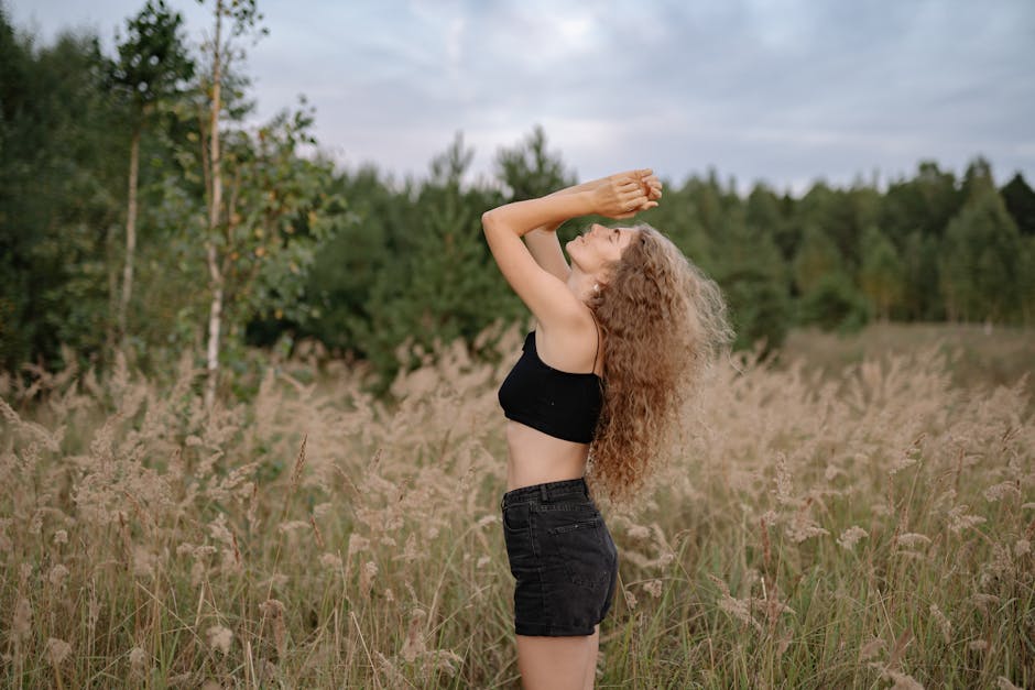 Side view of a carefree woman with curly hair embracing nature in a grassy field.