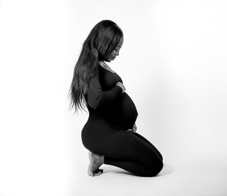 Pregnant woman kneeling in profile, portraying tranquility and expectation in black and white.