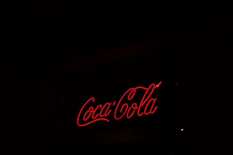 A bright neon Coca-Cola sign stands out against a dark background, shining vividly.