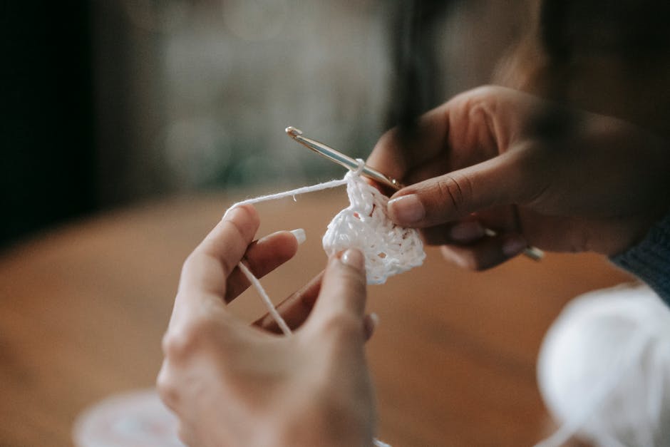 Detailed close-up of hands crocheting with a crochet hook and white yarn.