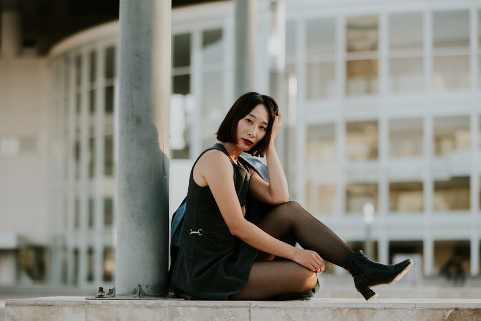 Elegant woman sitting by modern building, capturing urban fashion vibe.