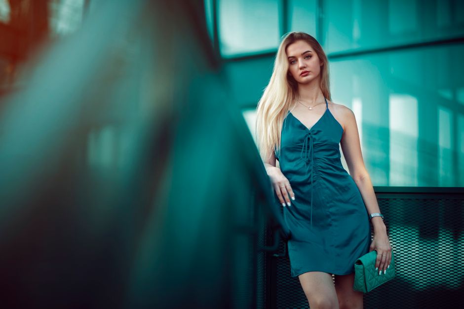 Portrait of a blonde woman in a blue dress standing near a modern building.