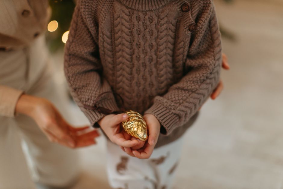 A child in a cozy sweater holds a golden ornament, evoking warmth and holiday cheer.