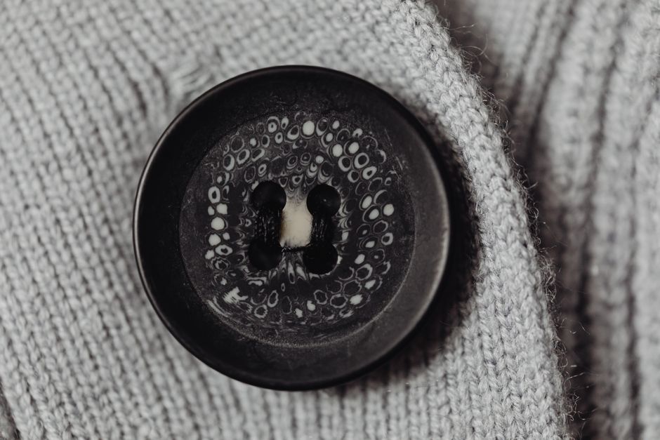 Detailed macro shot of a black button sewn on gray knitted fabric, showcasing texture.