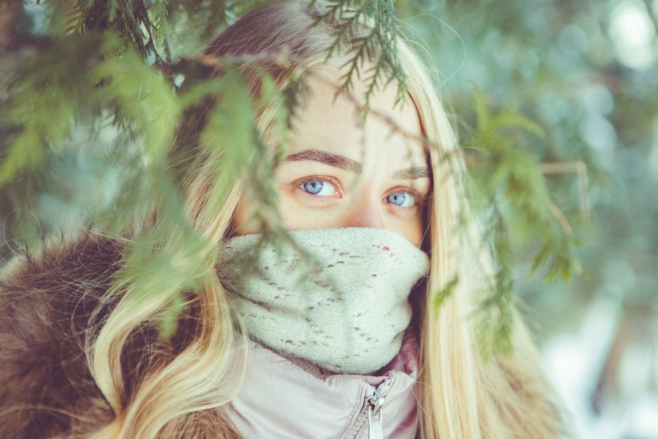 Close-up of a woman with blue eyes, wearing a scarf amidst winter foliage.
