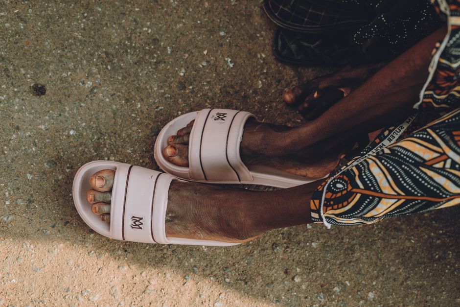 Close-up of feet wearing white sandals on textured ground.