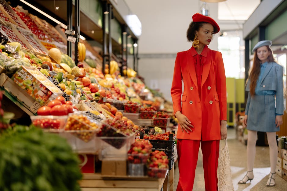 Fashionable women exploring a vibrant fruit market, showcasing elegant attire and colorful produce.