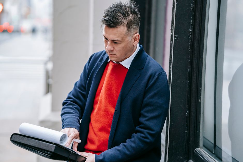 Professional man in a red sweater and suit reviewing paperwork outside during the day.