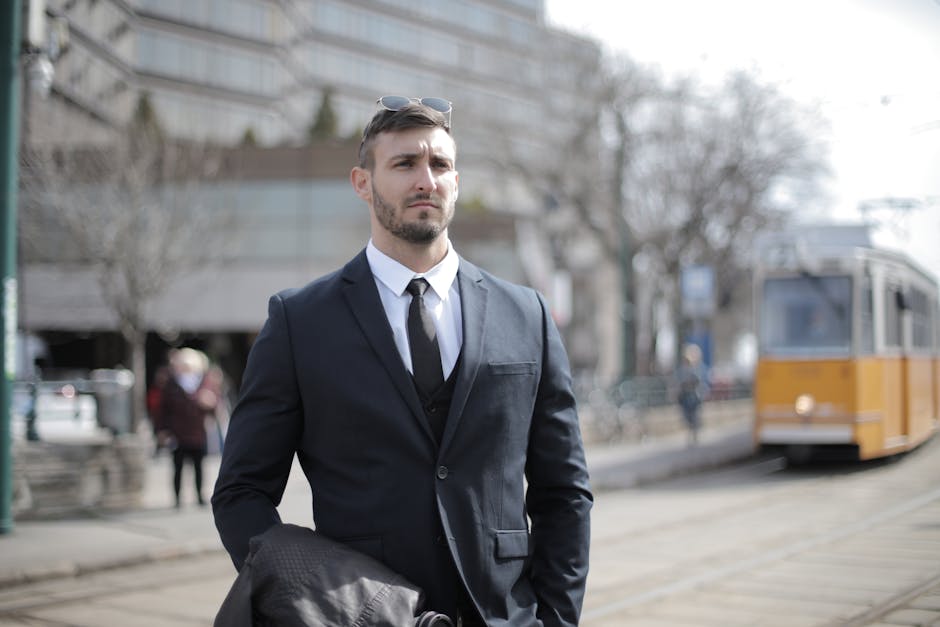 A serious businessman in a suit stands outdoors near a tram track.