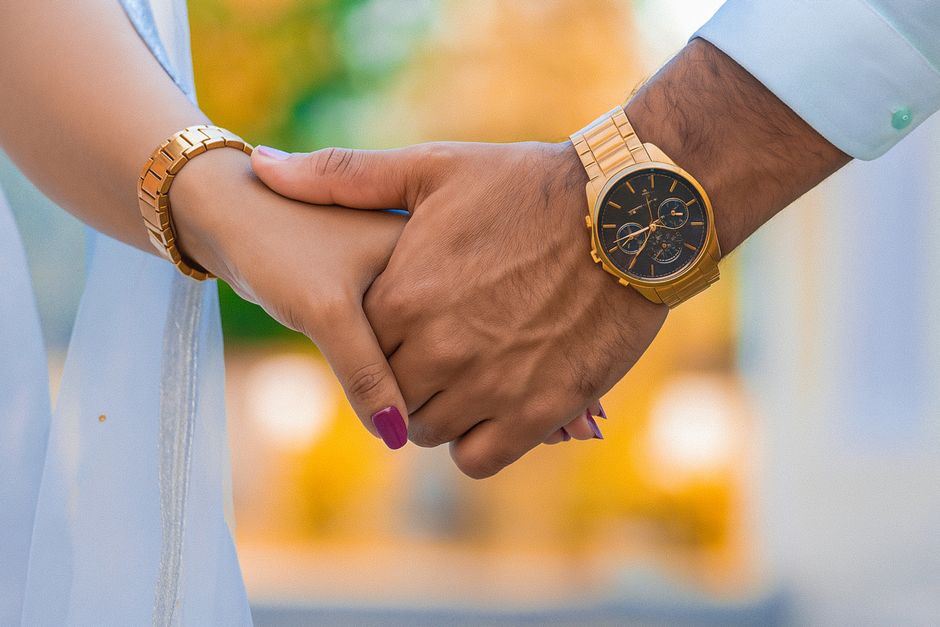 A close-up of a couple holding hands, both wearing matching gold watches, symbolizing love and connection.