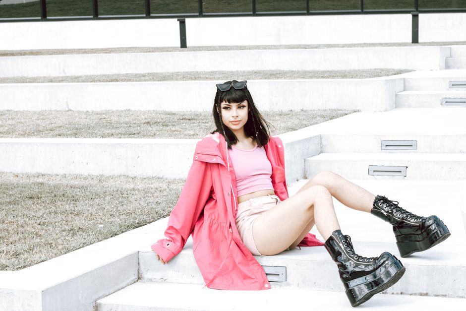 Stylish woman wearing pink jacket and platform boots sitting on outdoor stairs, exuding modern fashion.
