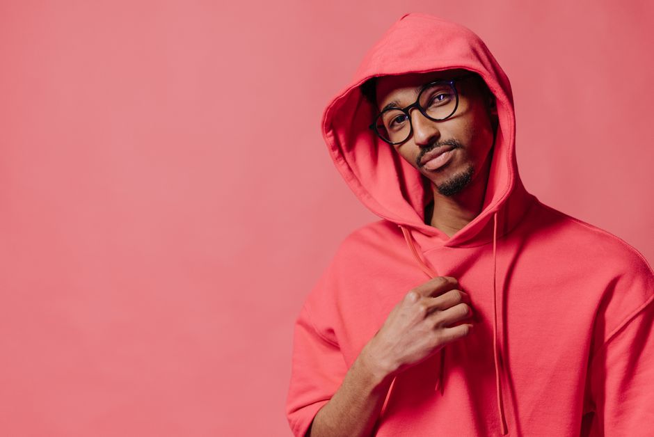 Portrait of a confident man wearing a red hoodie and eyeglasses against a red background. Studio shot.