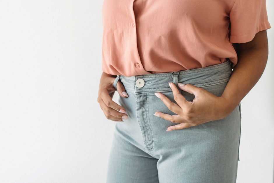 A close-up shot of a woman wearing a pink shirt and blue jeans on a white background.