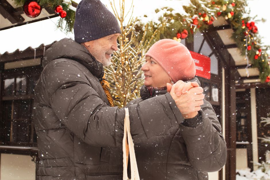 Smiling elderly couple in winter coats holding hands outdoors in the snow.