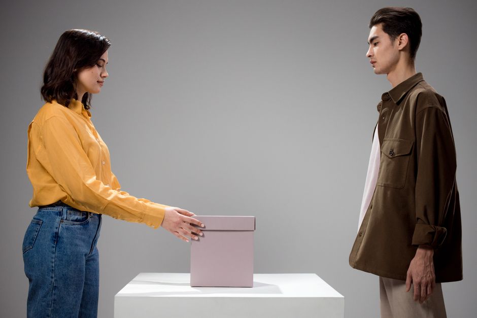 A man and woman standing opposite each other in a studio with a gift box in between.
