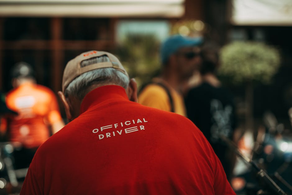 Man in red 'Official Driver' shirt at outdoor gathering. Captured from behind, showcasing event atmosphere.