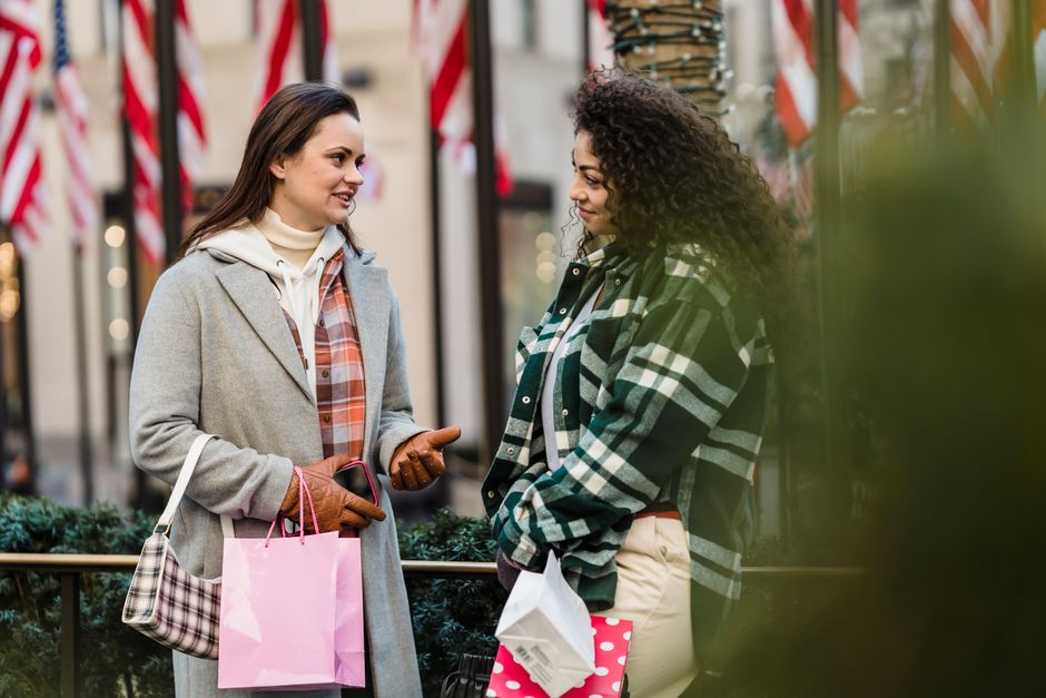 Content young multiethnic female friends in stylish clothes with shopping bags in hands communicating while standing on city street