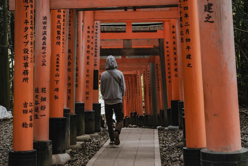 Person walking through iconic orange torii gates at Fushimi Inari Shrine in Kyoto, Japan.