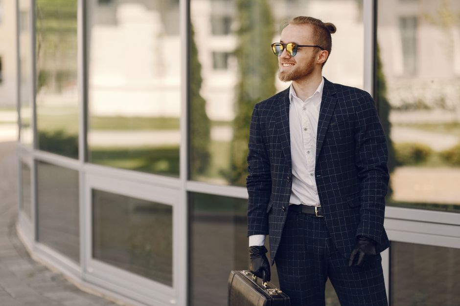Portrait of a confident businessman with a beard and sunglasses holding a briefcase outdoors.