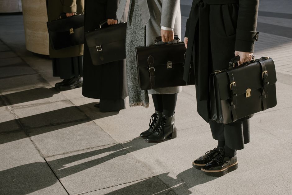 Row of business professionals holding leather briefcases outdoors.
