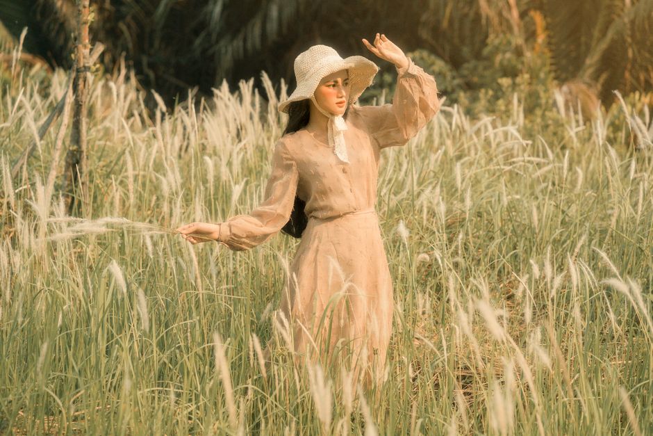 From above of young female in old fashioned dress and hat standing with raised arm with spikes while looking away in countryside