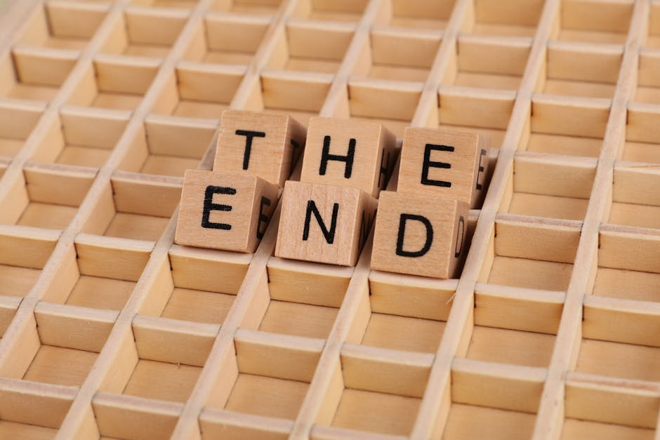 Close-up of wooden blocks spelling 'The End' placed on a wooden grid pattern surface.