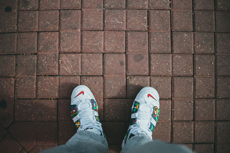 Top-down view of trendy white sneakers with colorful design on a red brick walkway.