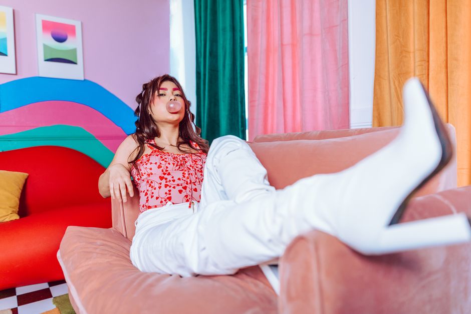 A stylish young woman blowing bubble gum while lounging on a colorful couch indoors.