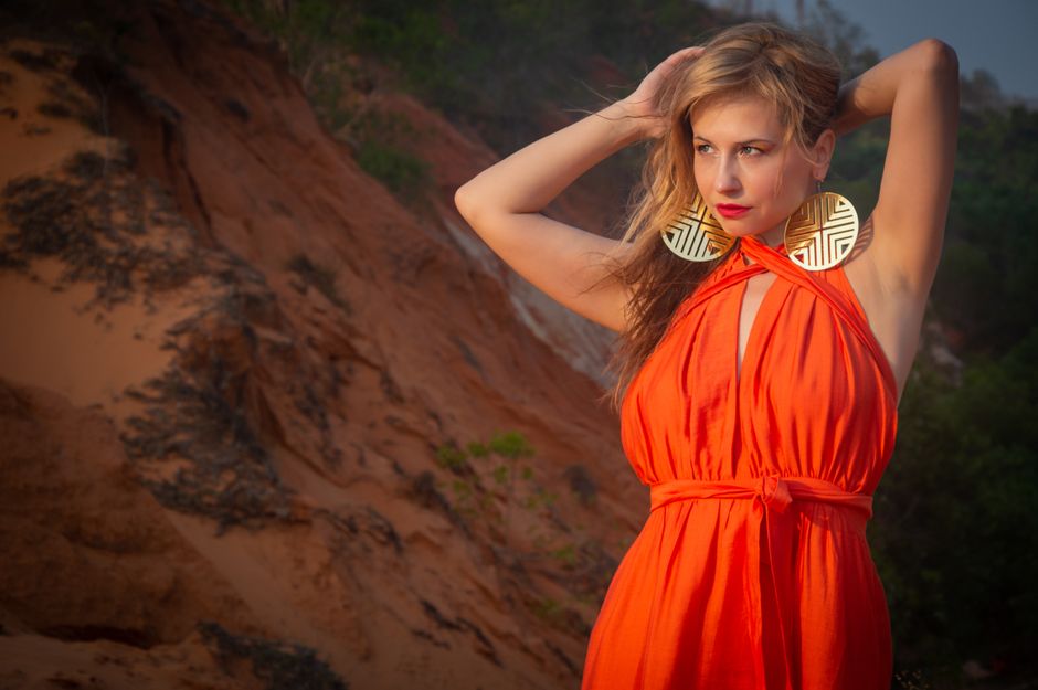 A fashionable woman in an orange dress posing confidently against a desert landscape.