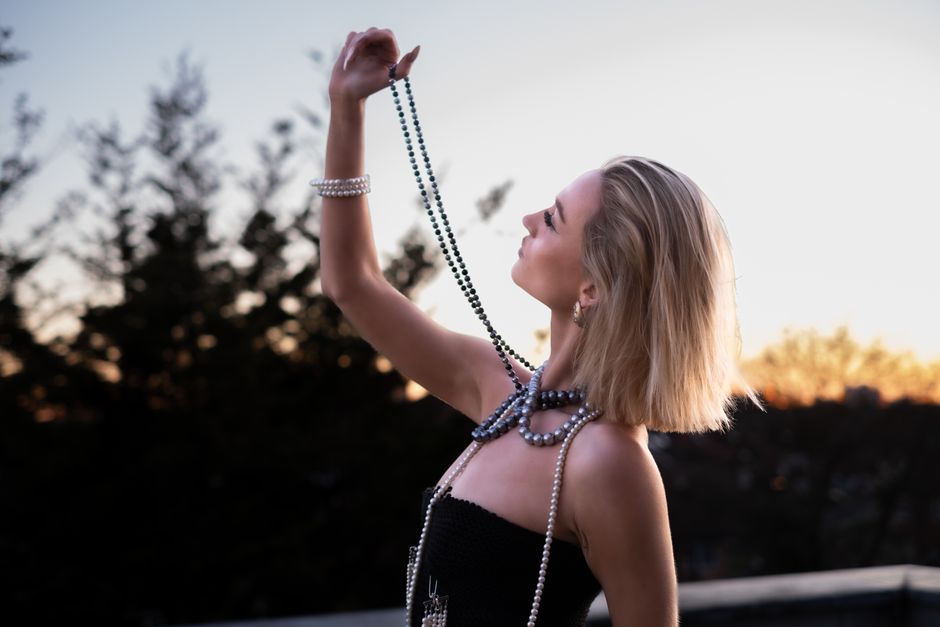 Profile of a stylish woman with pearl necklace against a sunset backdrop, exuding elegance and grace.