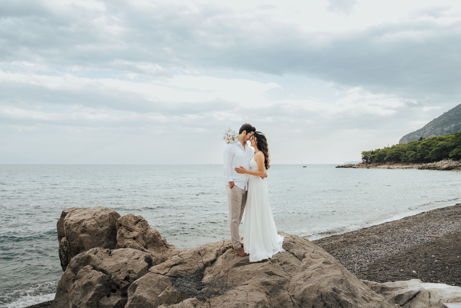 A couple embraces on rocky shores during a beach wedding in Antalya, Türkiye.