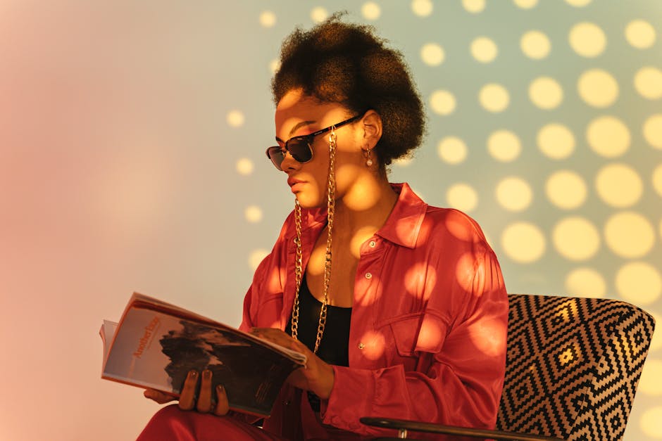 African American woman reading a book indoors with stylish sunglasses and dappled lighting.