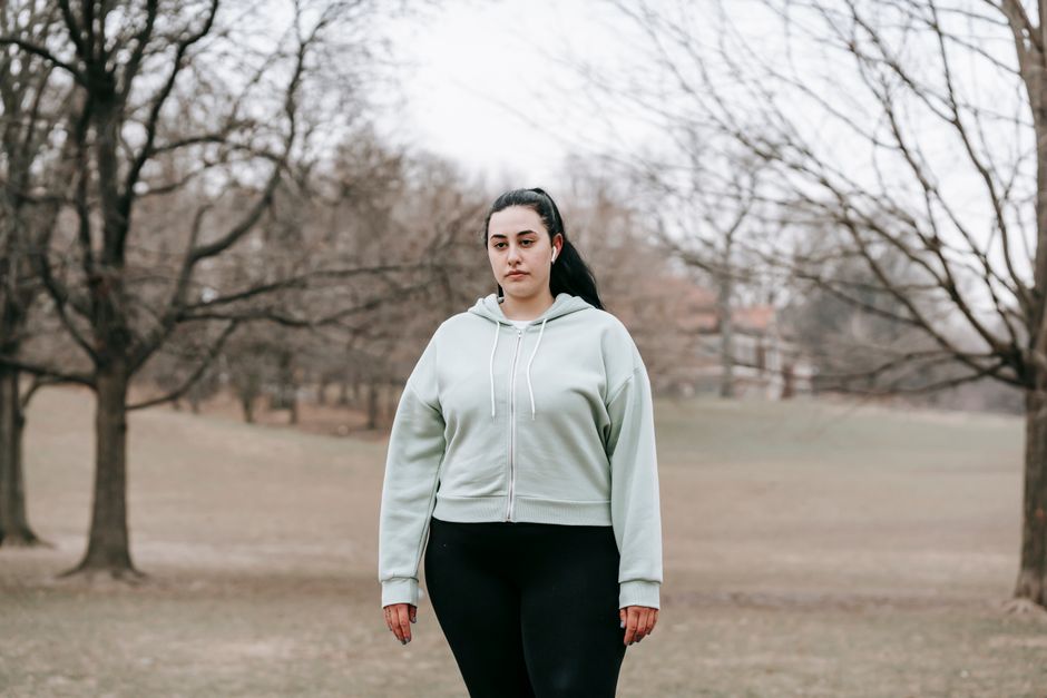 Young overweight female in activewear and earphones resting in autumn park on gloomy day