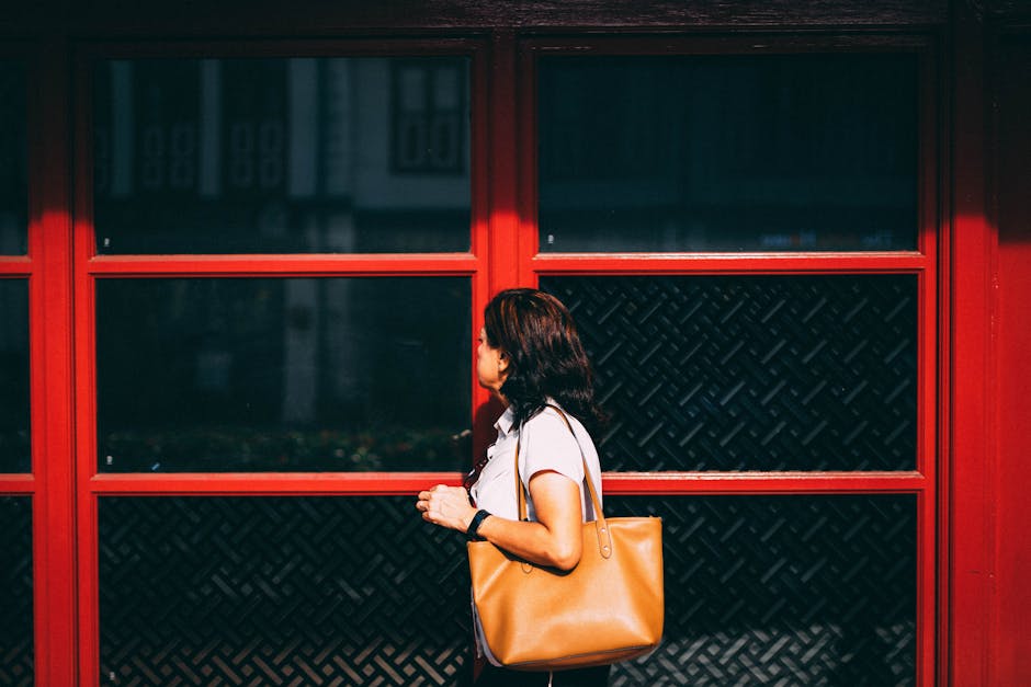 A woman with a tan handbag walks past a vibrant red storefront, capturing a candid urban moment.