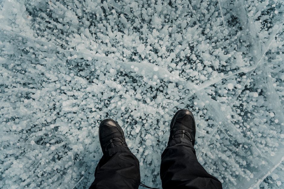 Top view of boots standing on uniquely patterned frozen ice with cracks.