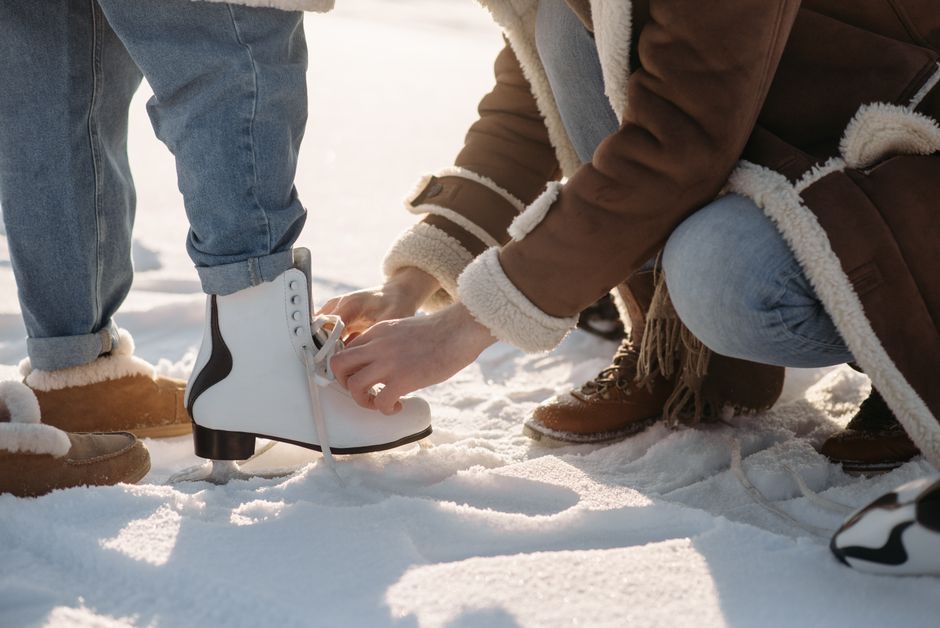 Hands tying ice skates on a snowy day, capturing a winter outdoor activity.